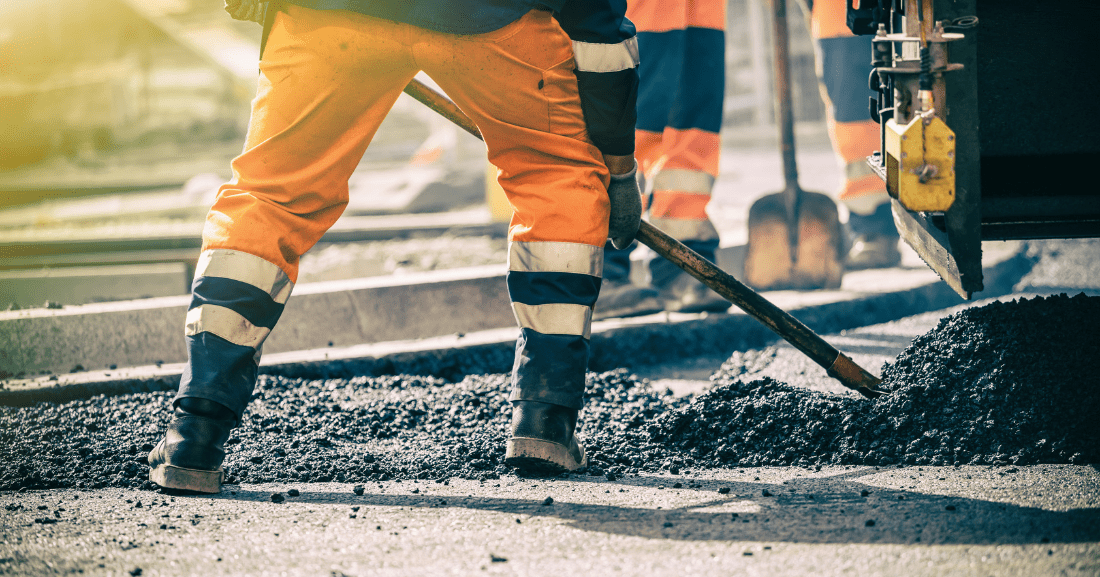 Travailleurs routiers en tenue haute visibilité en train de répandre et niveler de l’asphalte sur une route.