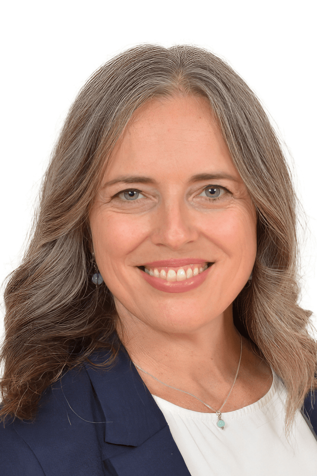 Portrait professionnel de Julie Lavoie, femme souriante aux cheveux longs poivre et sel, portant une chemise blanche, un veston bleu marine et un collier discret, sur fond blanc.