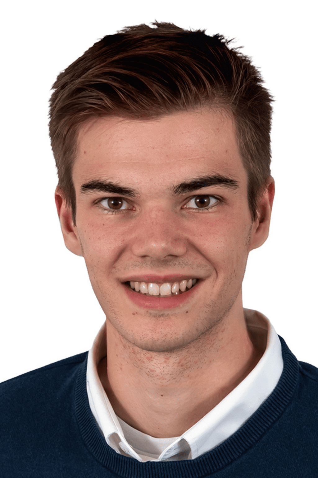 Portrait d’un jeune homme souriant portant une chemise blanche et un chandail bleu, devant un fond blanc.