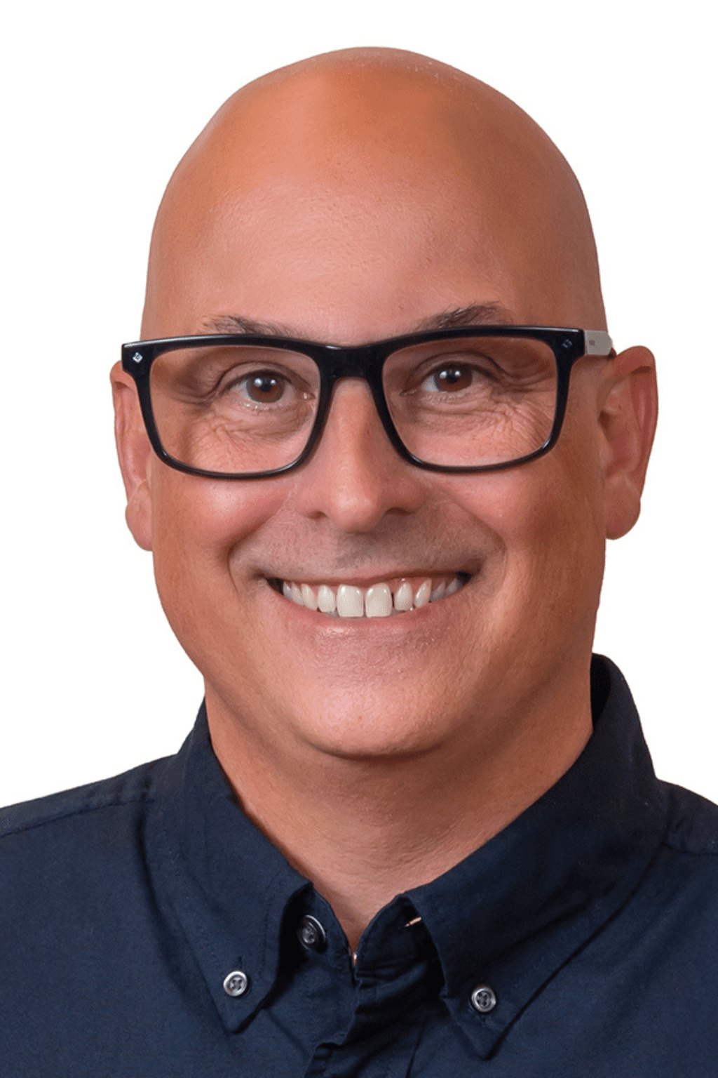 Portrait d’un homme souriant portant des lunettes noires et une chemise foncée, devant un fond blanc.