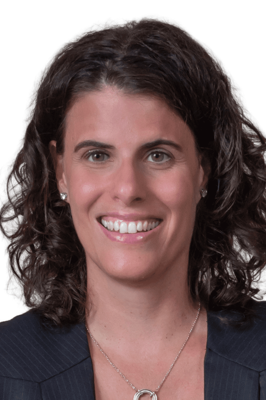 Portrait d’une femme souriante aux cheveux bruns et bouclés, portant un veston foncé et un collier argenté, devant un fond blanc.