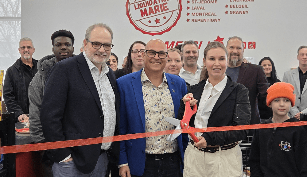 Cérémonie d’inauguration dans un commerce Liquidation Marie : une femme coupe un ruban rouge avec de grands ciseaux, entourée d’un groupe de personnes souriantes.