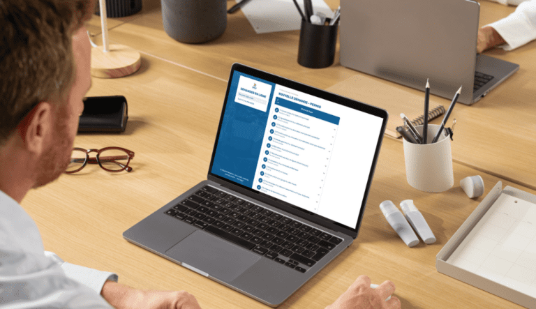 Personne utilisant un ordinateur portable affichant un formulaire de demande en ligne sur un bureau.