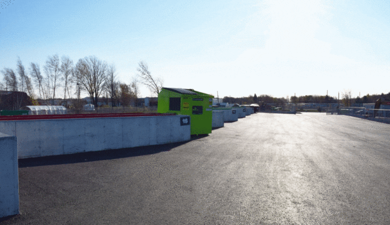 Vue extérieure d’un écocentre municipal avec des conteneurs alignés sur une aire asphaltée.
