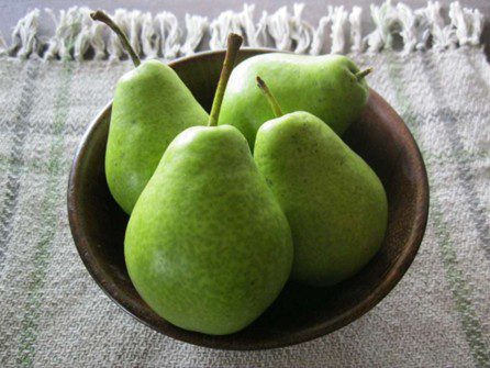 Poires vertes de Pyrus ‘Ste-Sophie’ présentées dans un bol en bois.