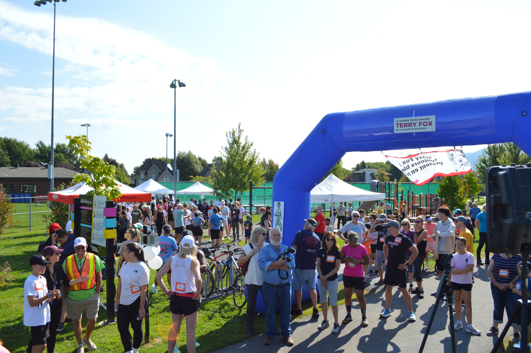 Participants rassemblés sous une arche de la Fondation Terry Fox lors d’un événement communautaire extérieur de marche ou de course.