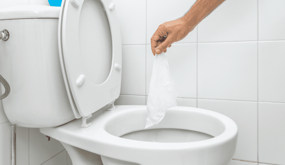 Main tenant une lingette au-dessus d’une toilette ouverte.