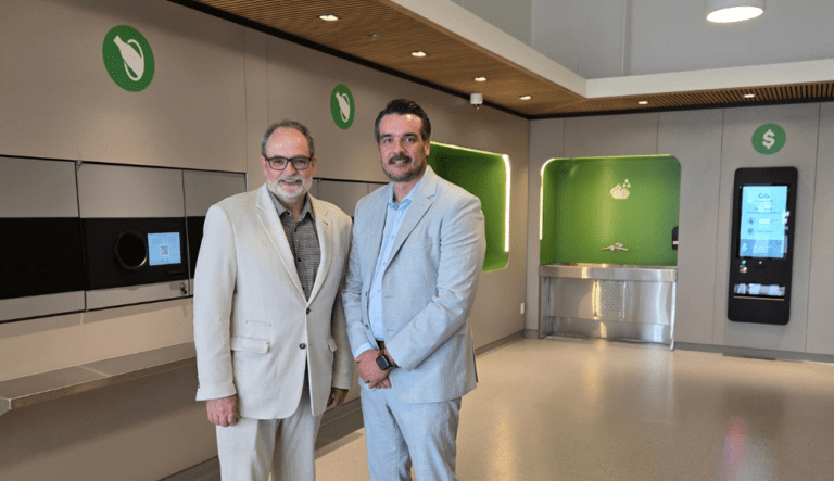 Deux hommes en complet clair posent dans un espace moderne équipé de stations de tri, de récupération et de services automatisés.