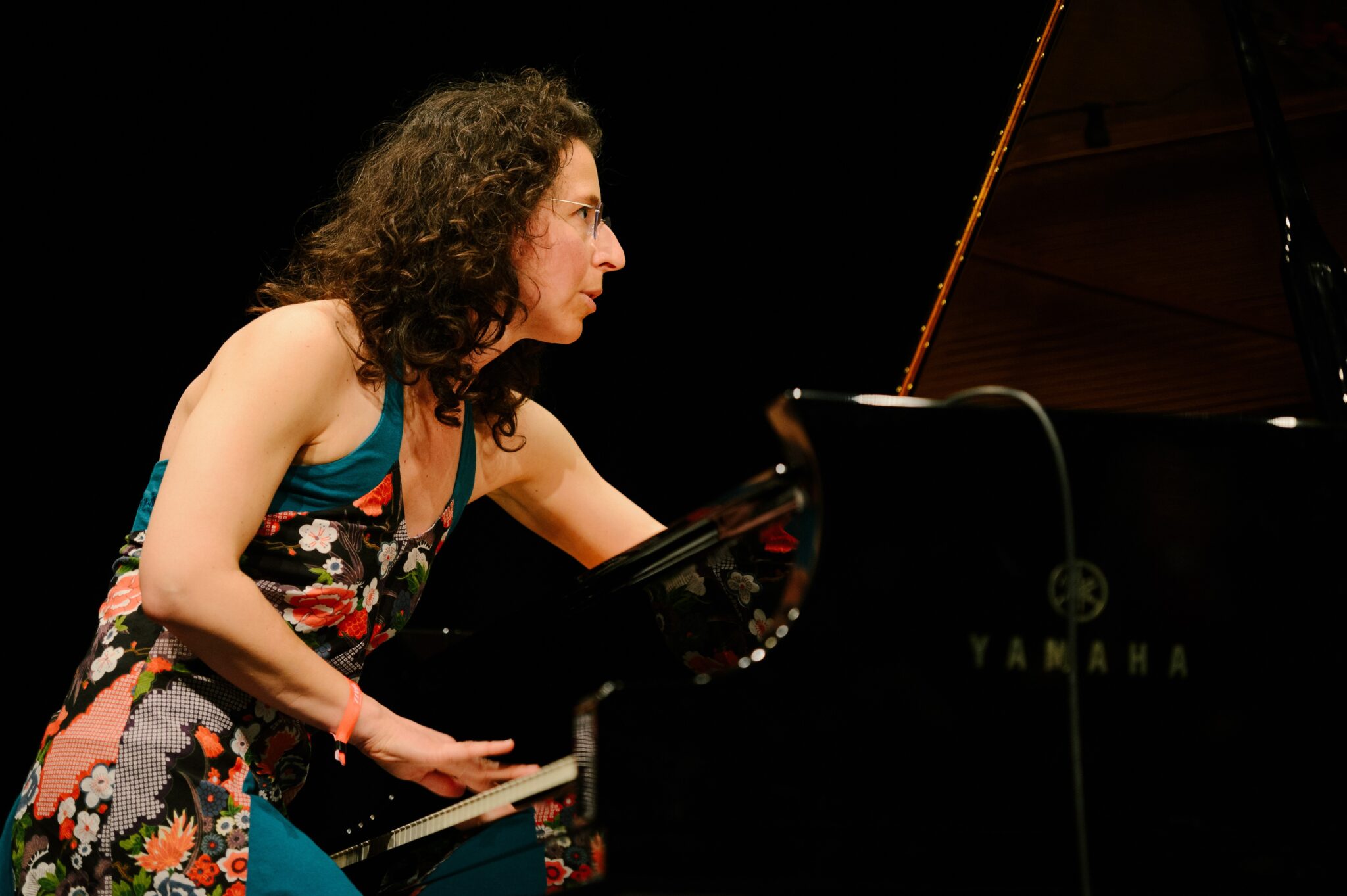 Personne jouant du piano à queue sur une scène, photographiée de profil pendant une prestation musicale.