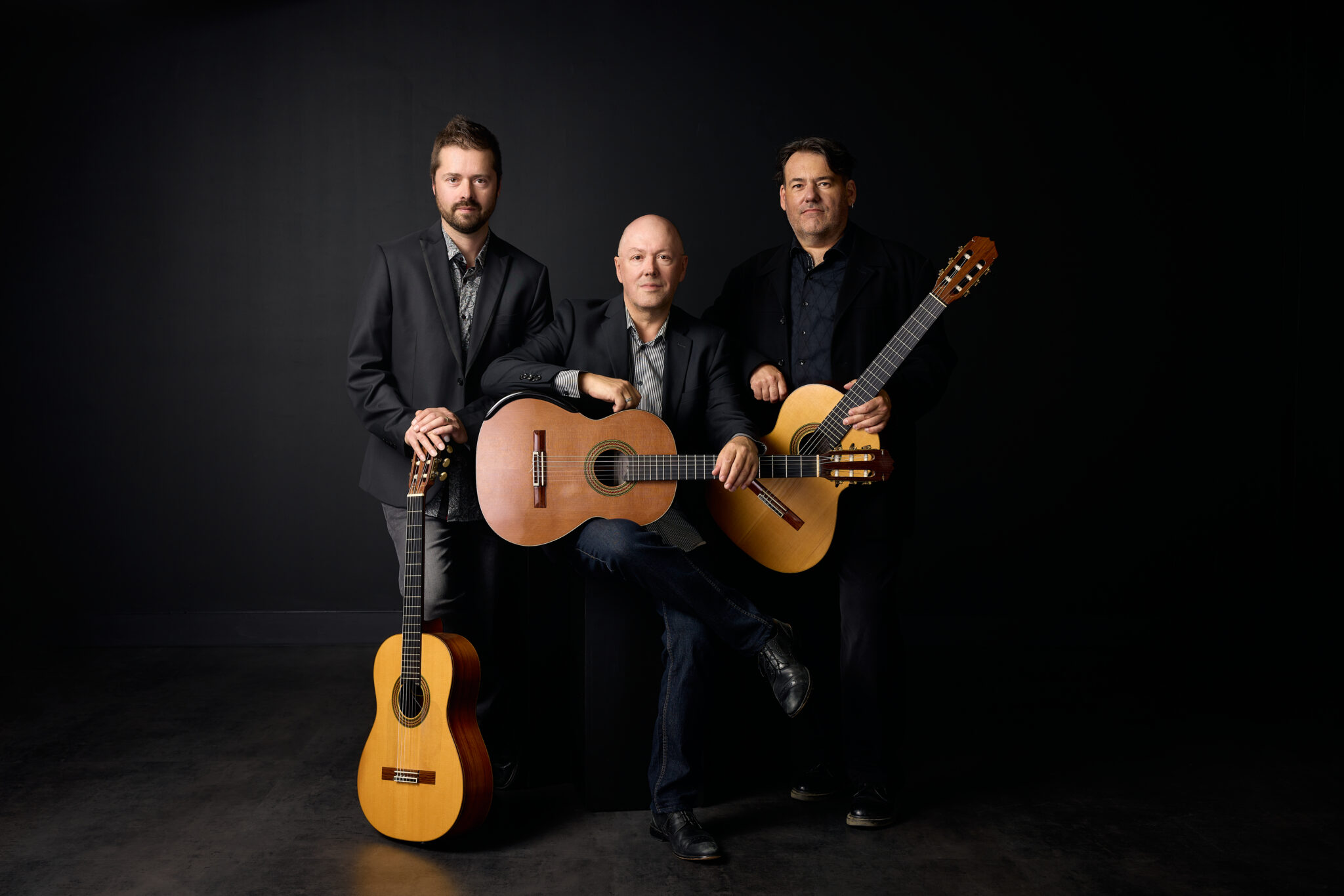 Trois musiciens posent avec des guitares classiques devant un fond noir dans un portrait promotionnel.