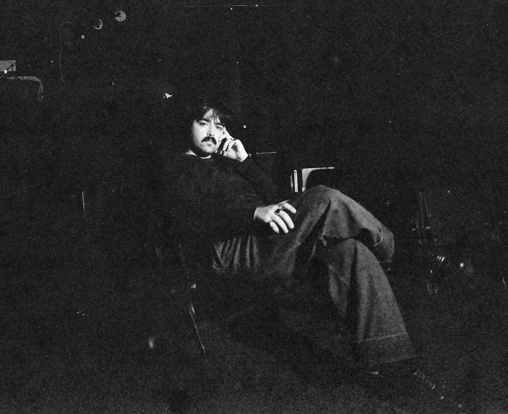 Portrait en noir et blanc d’une personne assise dans un fauteuil dans un environnement sombre, photographiée dans une composition à faible éclairage.