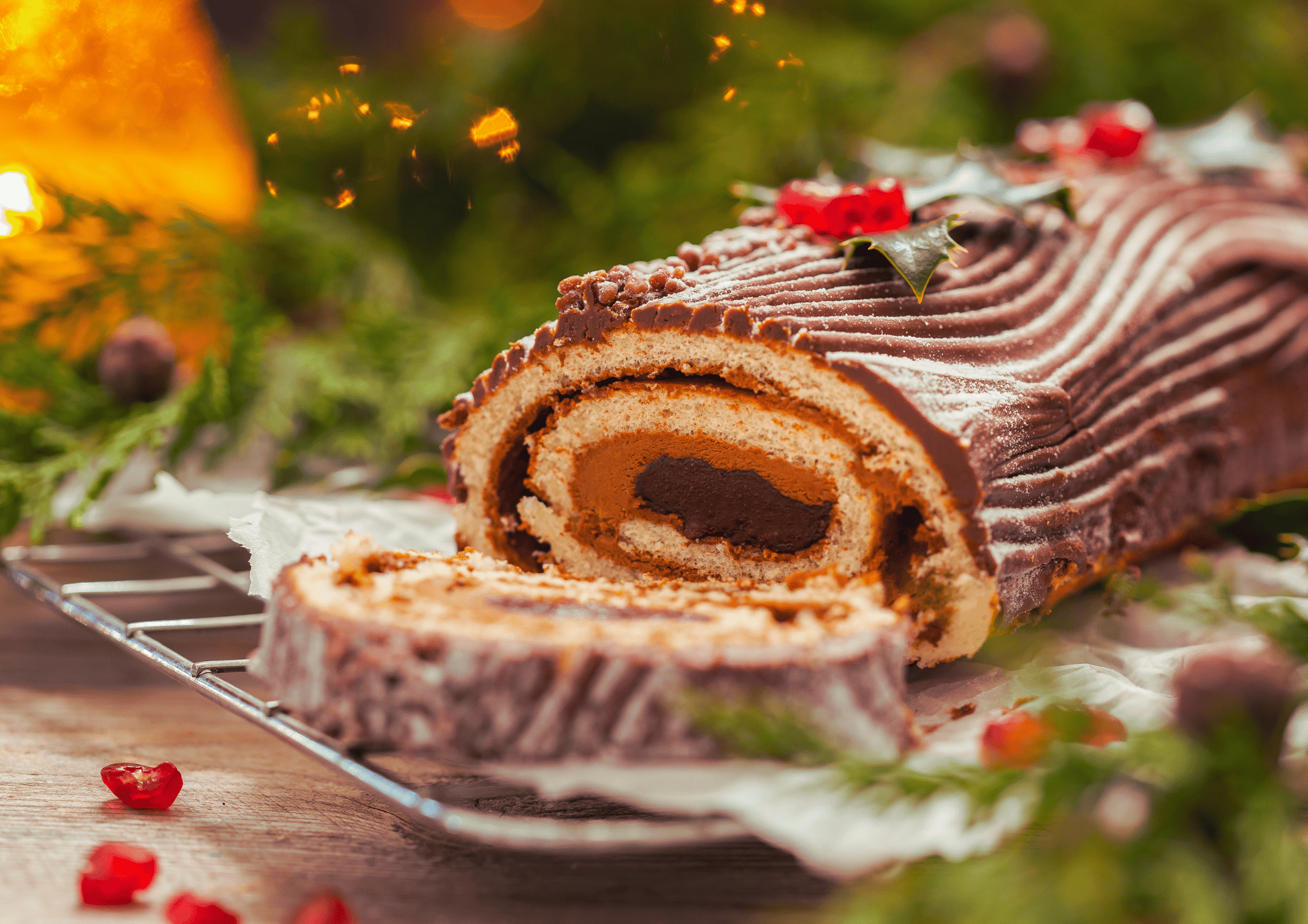 Bûche de Noël au chocolat garnie de sucre à glacer, présentée sur une grille de refroidissement et décorée de feuilles de houx et de petits fruits rouges.