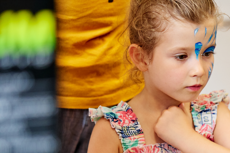 Enfant participant à une activité de maquillage, avec un motif bleu peint sur le visage.