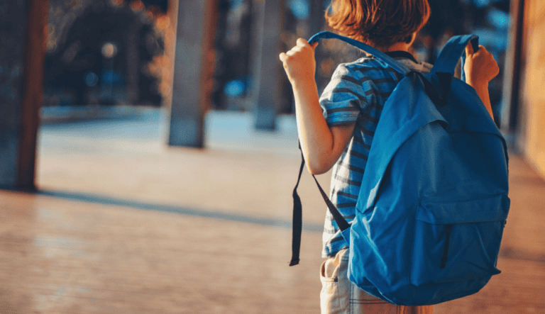 « Enfant de dos ajustant les bretelles d’un grand sac à dos bleu dans un corridor d’école. »